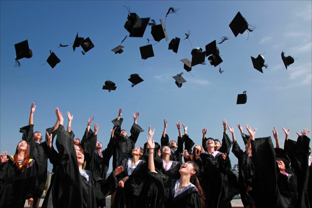 About Group of graduates celebrating by throwing caps in the air during a sunny day.