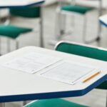 Cennik A close-up of an empty classroom desk with exam papers and a pencil, highlighting education and testing environment.