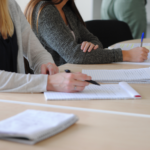 Cennik Group of students writing notes at a meeting in a well-lit classroom.
