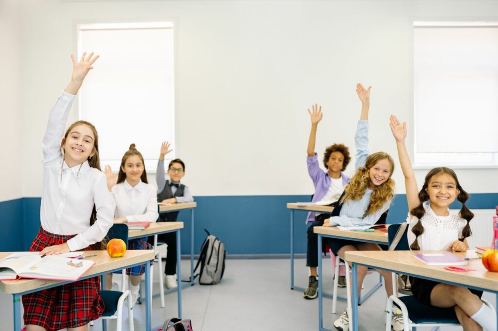 pexels photo 8617994 8617994 Group of diverse children eagerly raising hands in a bright classroom setting.